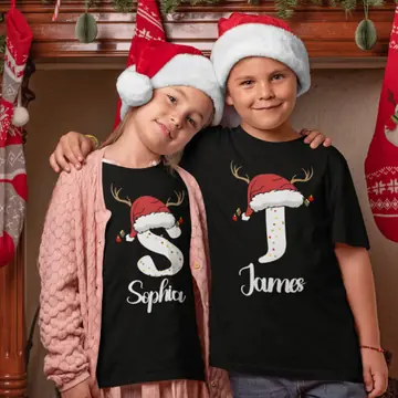 Two children in black Christmas shirts with S and J initials, wearing Santa hats